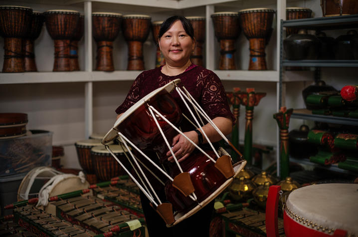 Donna Kwon holding a drum in a room filled with various instruments
