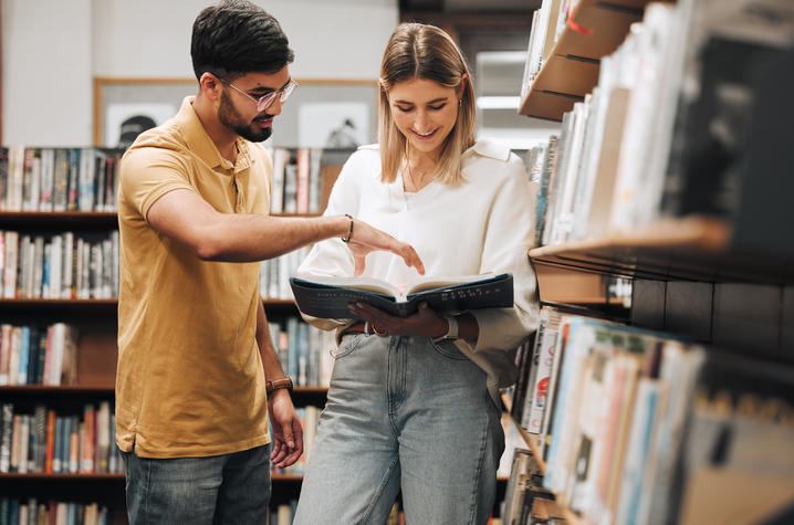 two people looking over a book in a library