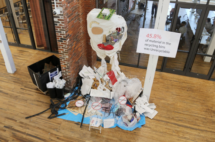 an art display created with recycled materials and a sign reading "45.8% of material in the recycling bins was unrecyclable"