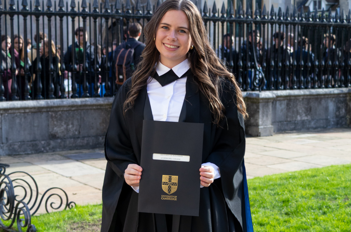 Gretchen Ruschman in graduation regalia, holding a degree from Cambridge University 