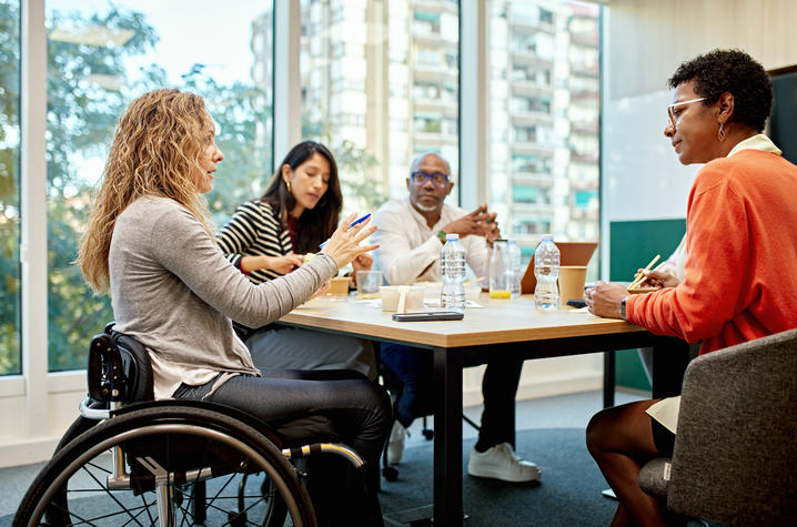 a group of coworkers meet at a table, one of them uses a wheelchair
