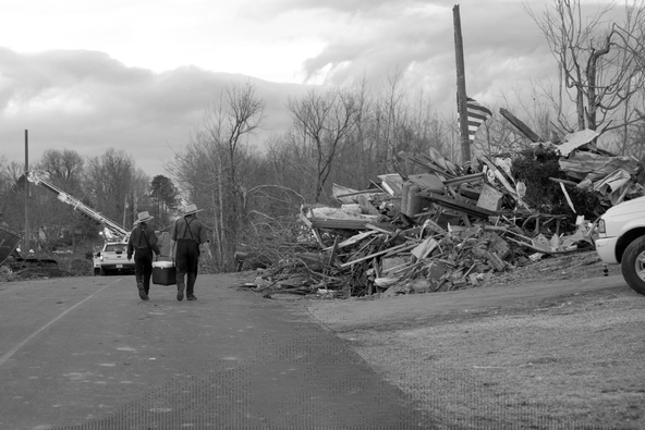 two people carrying a cooler walk by a mound of debris left after a storm