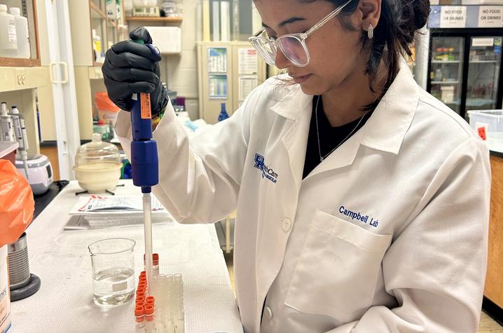 a student in a white lab coat and PPE fills test tubes with a liquid