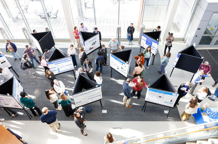 attendees at a poster session inspect triangular poster board displays in the atrium of a large building