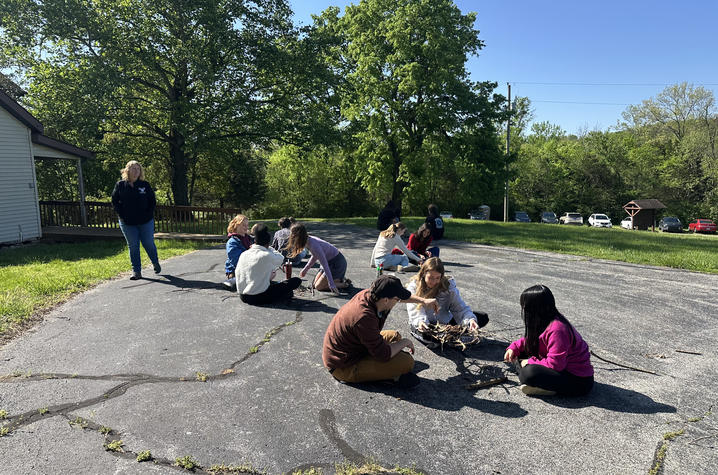 Students sit on the ground outside, working together in small groups