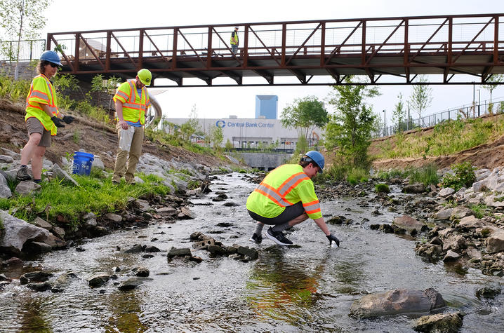 researchers take water samples from Town Branch flowing under a bridge