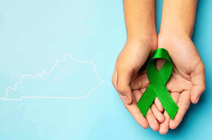 hands holding a green ribbon next to an outline of the state of Kentucky