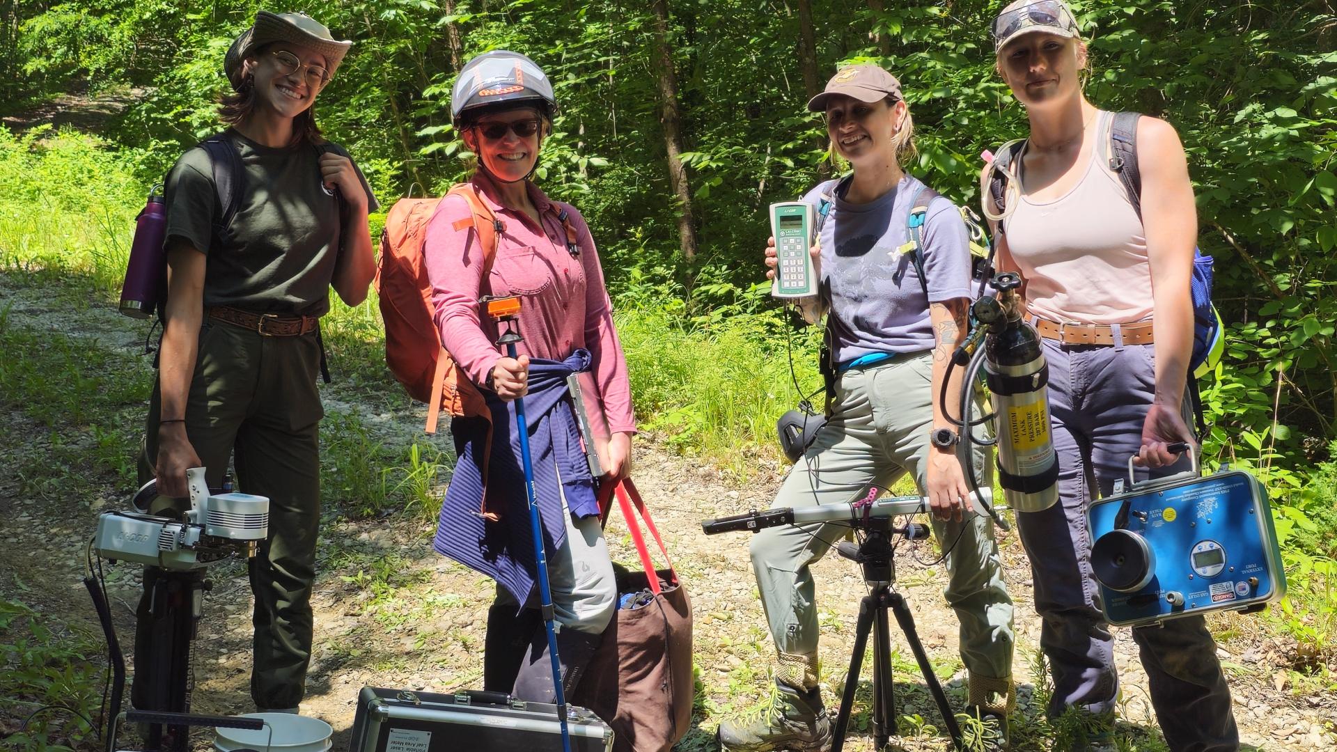 researchers hold equipment near a trail in a wooded area