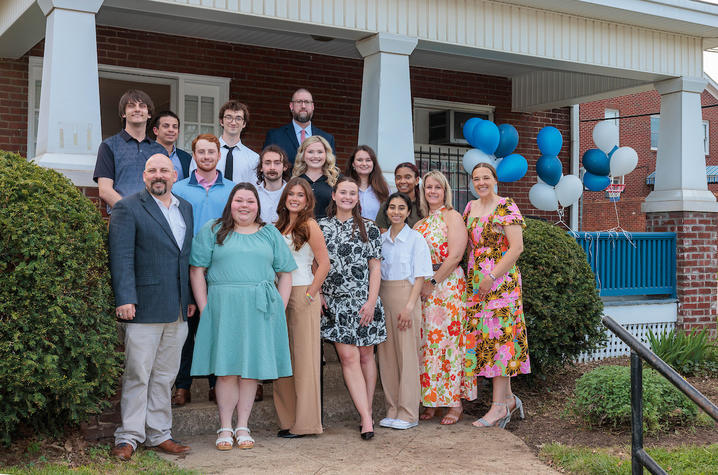 A group of people pose outside a brick building entrance decorated with blue and white balloons.