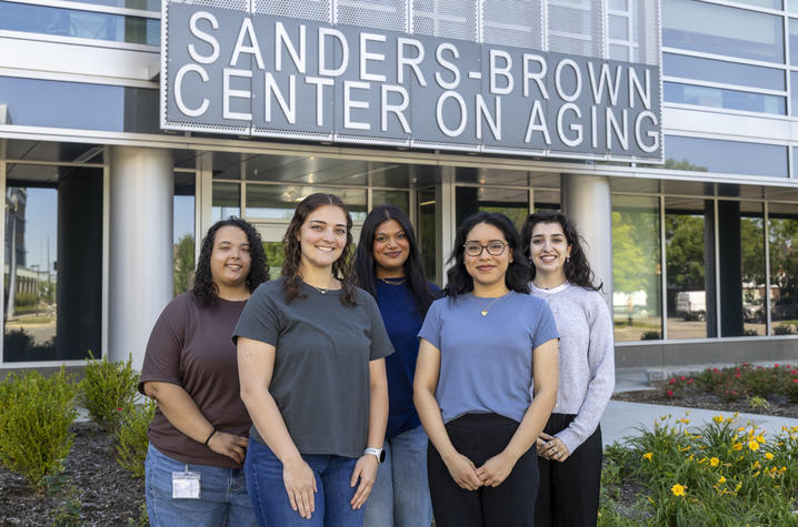 Five students stand together outside the Sanders-Brown Center on Aging, smiling for a group photo beneath the center’s sign.