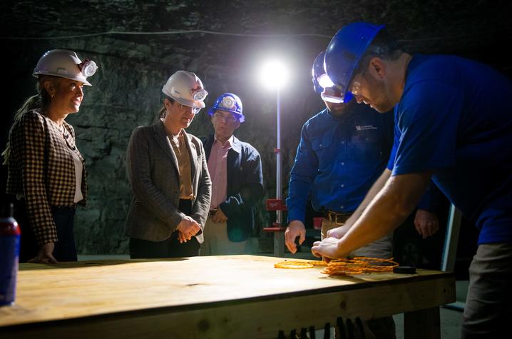 People wearing hard hats gather around a table during a demonstration inside an underground mine.
