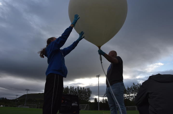 Two people holding a weather balloon in a dark, outdoor setting.