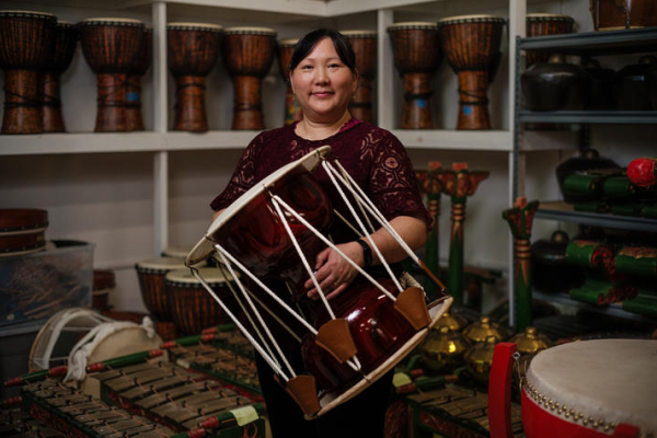Donna Kwon holding a drum in a room filled with various instruments