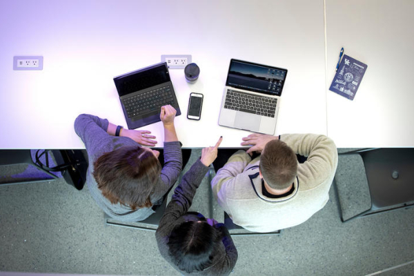 students sitting at a desk, working on laptop computers