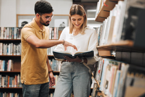 two people looking over a book in a library
