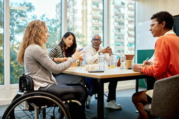 a group of coworkers meet at a table, one of them uses a wheelchair