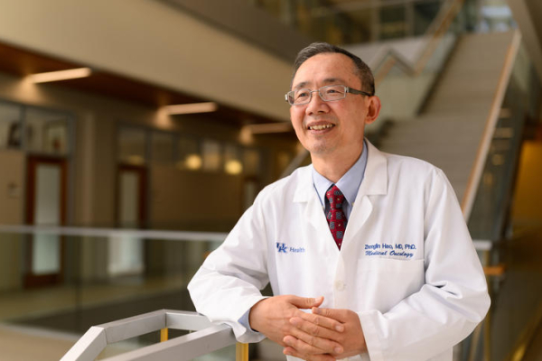 Zhonglin Hao stands near a stairway while wearing a white lab coat