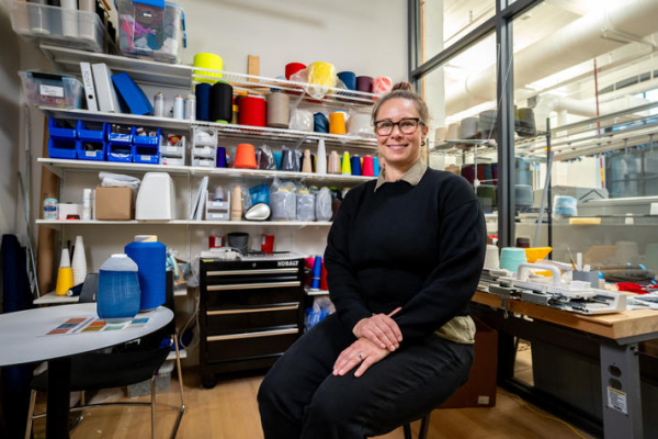 Jennifer Meakins sits in a studio space surrounded by colorful spools of thread
