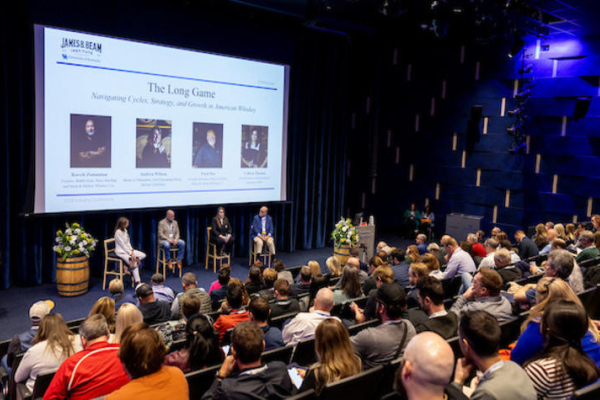 a panel of people sitting under a presentation screen at the front of an auditorium full of spectators