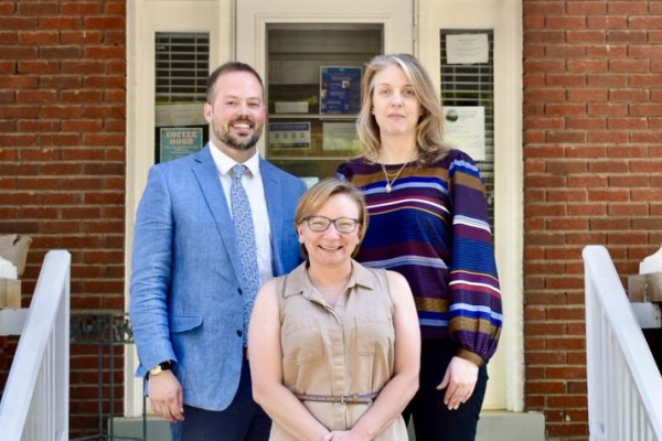 Austin Zinkle, Kathryn Engle and D’lorah Hughes stand on a stairway in front of a door