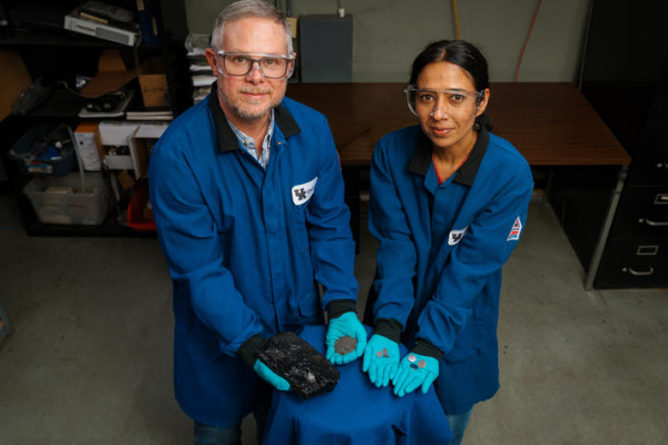 researchers in blue lab coats hold coal, graphite, electrodes and batteries
