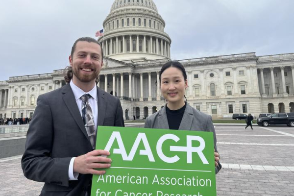 Subin Kim and another researcher hold a sign for the American Association for Cancer Research in front of the U.S. Capitol building