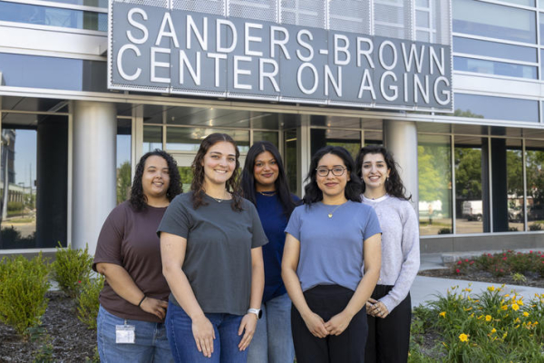 Five students stand together outside the Sanders-Brown Center on Aging, smiling for a group photo beneath the center’s sign.