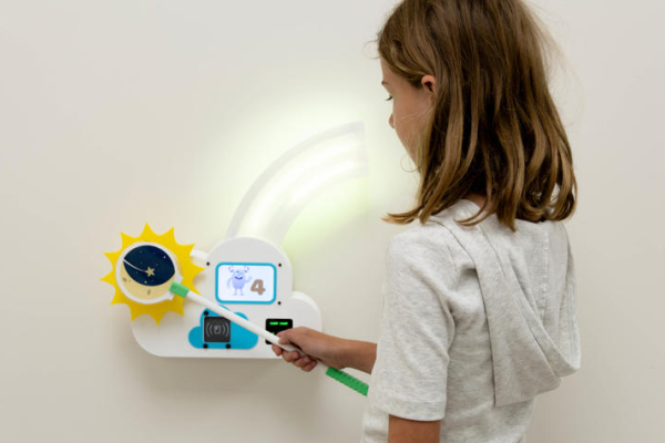 A child uses a moon-themed wand at a lighted wall-mounted game station displaying an animated character and the number four.