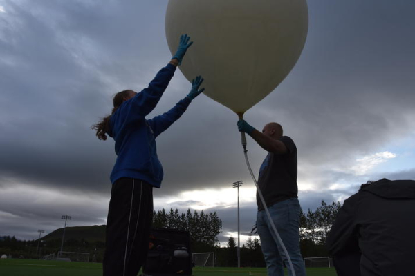 Two people holding a weather balloon in a dark, outdoor setting.