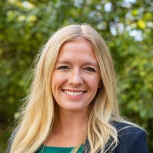 Image of Abigail Latimer, a white women with long blonde hair wearing a black blazer and green top.