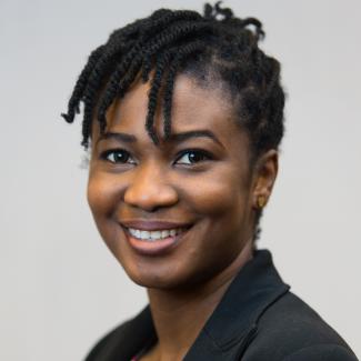 Image of Darlingtina Esiaka, a black women with black hair pulled up with dark eyes, wearing a colorful top with a black blazer