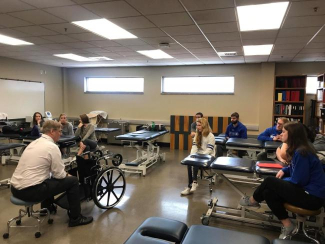A collection of students are listening to a teacher in the middle of a classroom dedicated to physical disability education