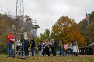 students gathered around a meteorology device outside while listening to a lecture