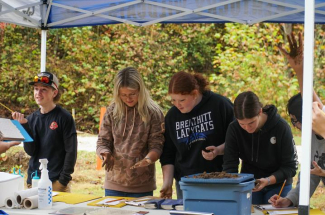 Students examining different soil types under a tent outside
