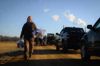 Haley Taylor carries bags with research materials next to a line of vehicles