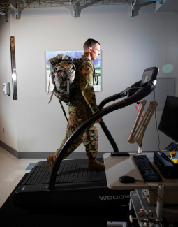 a person in military fatigues and a backpack walking on a treadmill in a lab 