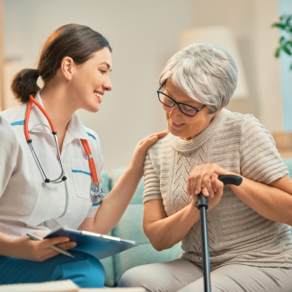 Clinician speaking with and supporting an older patient during a care visit in a home or clinical setting