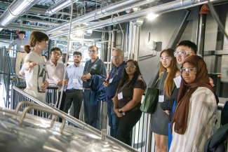 a group of people wearing safety goggles listening to a tour guide in a distillery