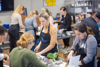 multiple people wearing aprons prep food in a large, commercial kitchen