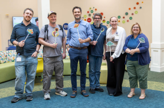 Members of a project team stand together in a pediatric clinic and hold colorful space-themed game wands.