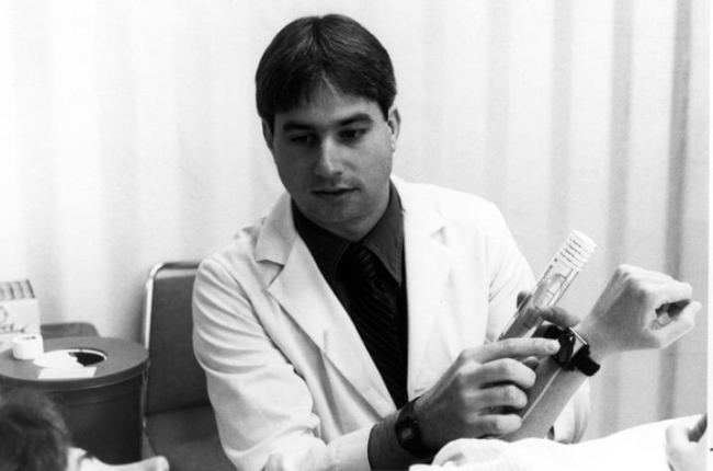 Daniel Wermelin, beside a patient in bed, explaining how to use a medical device