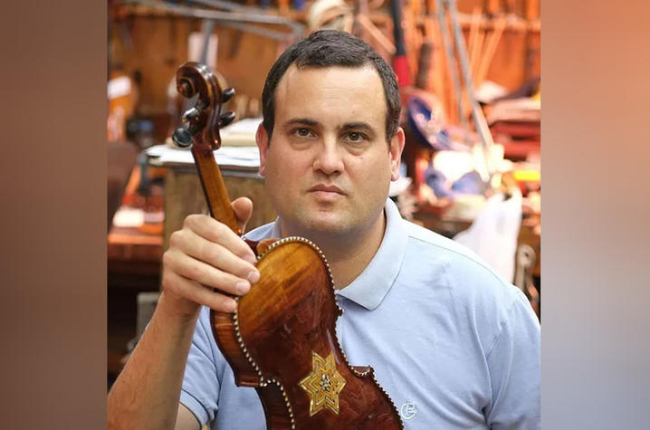 Avshalom Weinstein holds up a violin in a workshop